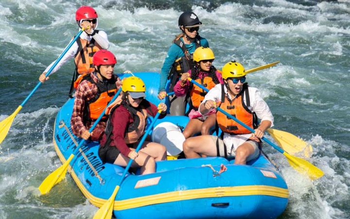 a group outward bound students use paddles as they guide a raft through whitewater 
